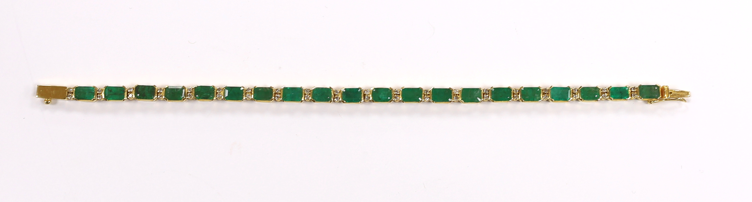 A modern 18k yellow metal and twenty stone emerald set line bracelet, with diamond chip spacers, 18cm, gross weight 13.5 grams.